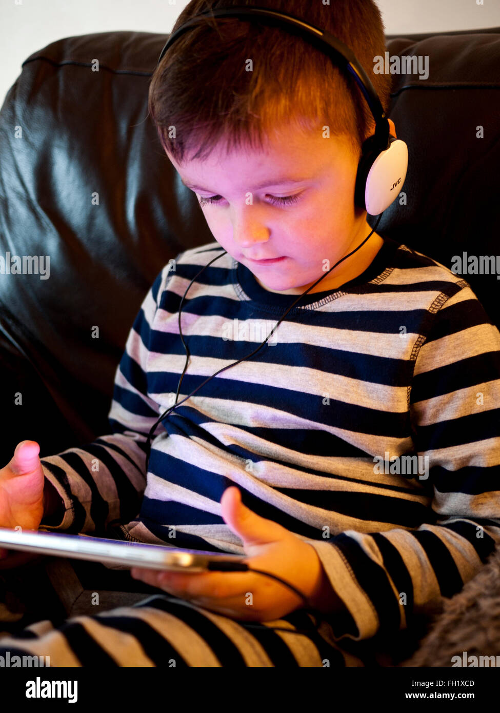 Young 5 year old boy using an i pad with ear phones, UK. Stock Photo