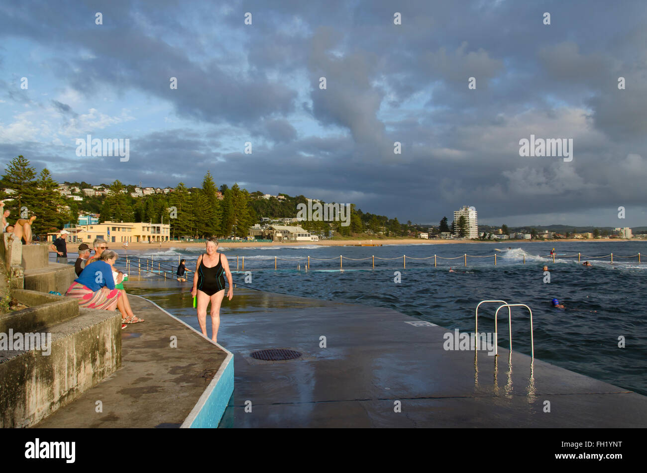 People sitting and standing beside an ocean pool at Sydney's Collaroy Beach early in the morning in Australia Stock Photo