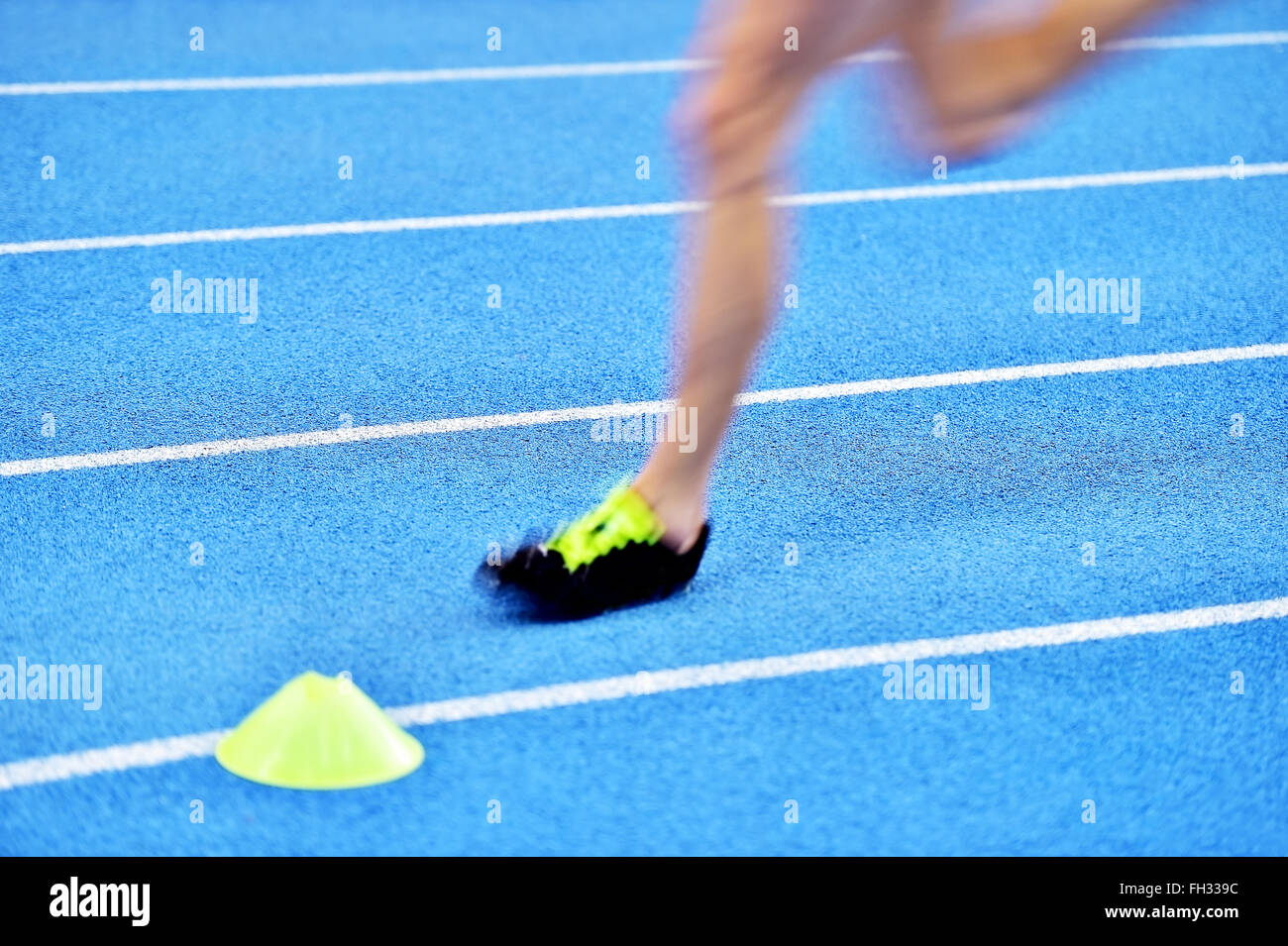 Blurred athlete by a slow camera shutter speed competing on blue sprint track Stock Photo