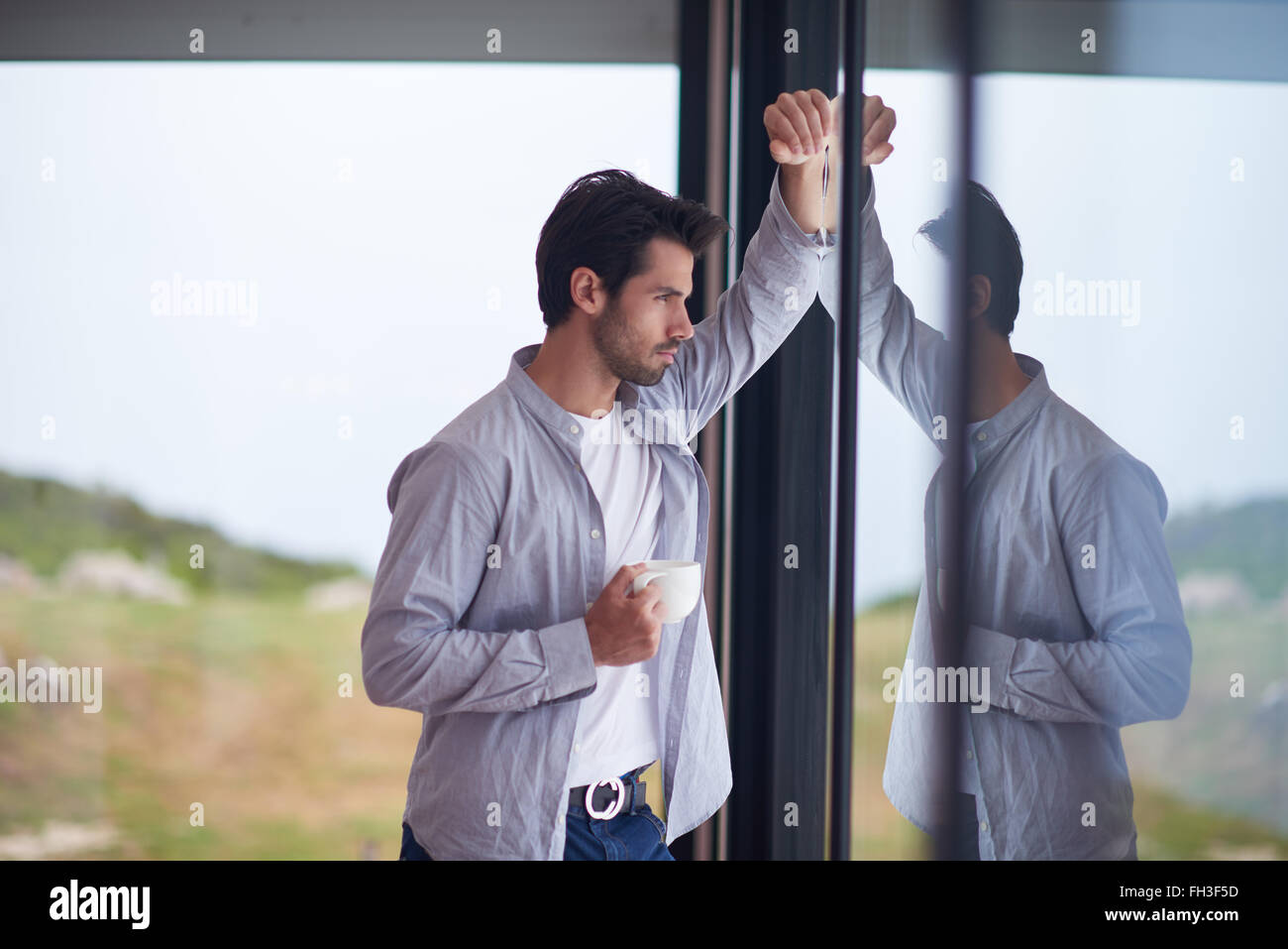 relaxed young man drink first morning coffee withh rain drops on window Stock Photo