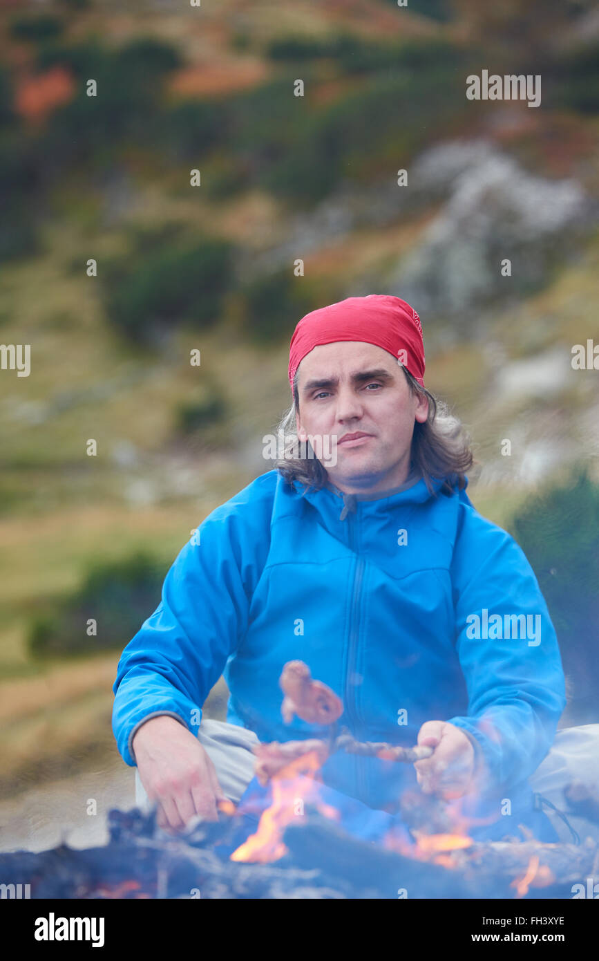 hiking man prepare tasty sausages on campfire Stock Photo