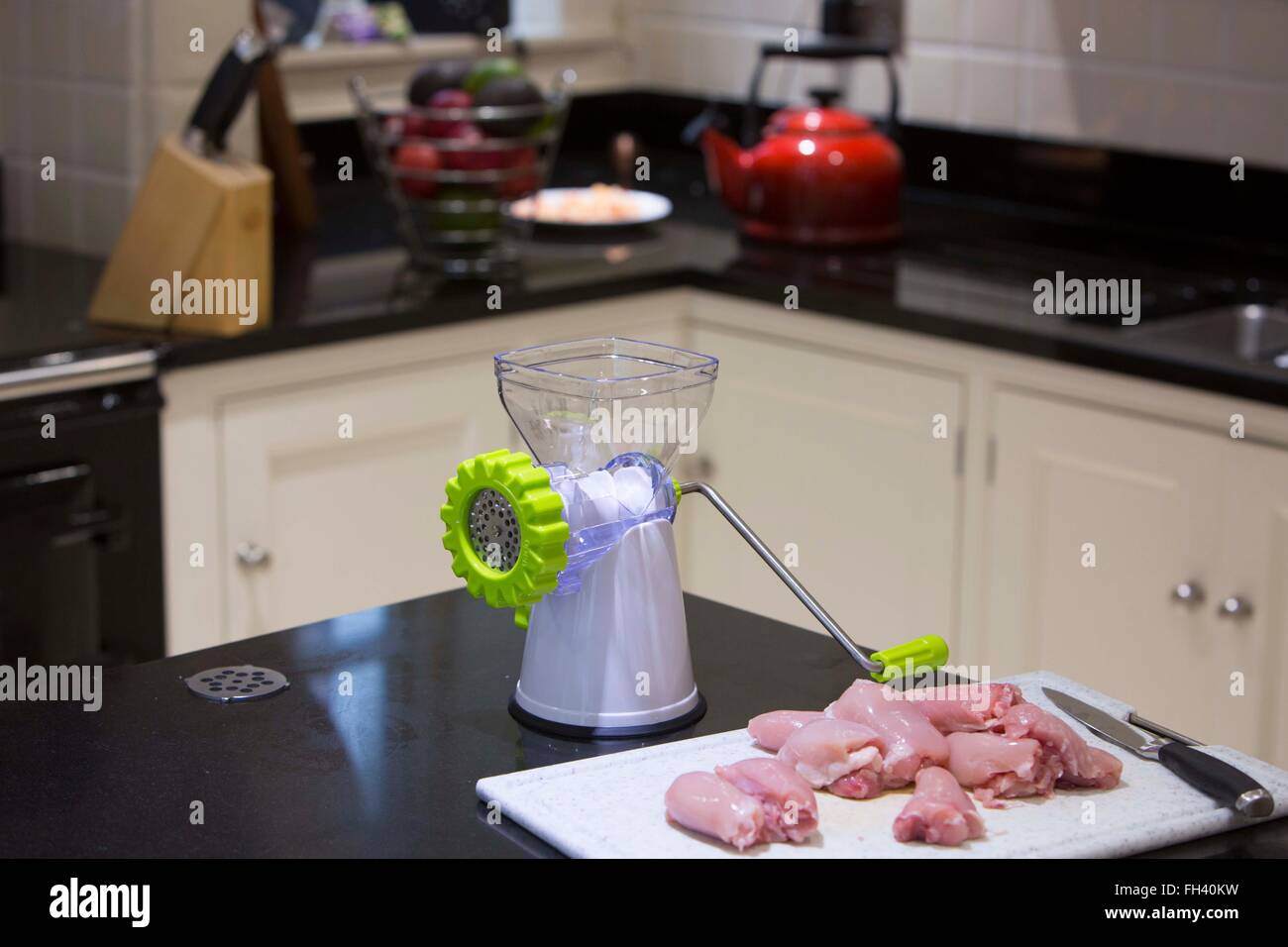 Chicken thighs on a chopping board on a granite work top in a family home kitchen next to a mincer. Stock Photo