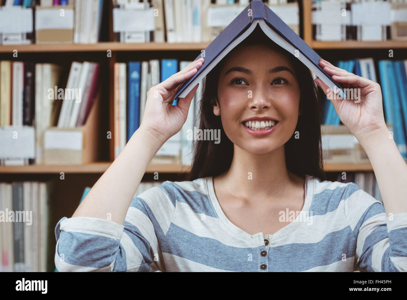 Funny student holding book on her head Stock Photo - Alamy