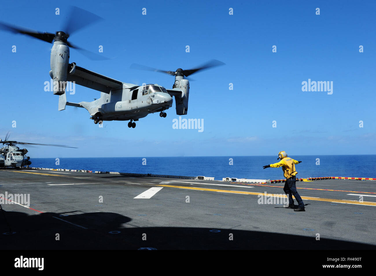 PACIFIC OCEAN (Feb. 22, 2016) Aviation Boatswain’s Mate (Handling) 3rd Class Demetri Cornett signals an MV-22 Osprey, assigned to Marine Medium Tilt Rotor Squadron (VMM) 166 (Reinforced), on the flight deck of amphibious assault ship USS Boxer (LHD 4). More than 4,500 Sailors and Marines from Boxer Amphibious Ready Group and the 13th Marine Expeditionary Unit (13th MEU) are conducting sustainment training off the coast of Hawaii in preparation for entering the U.S. 5th and 7th Fleet areas of operations. Stock Photo