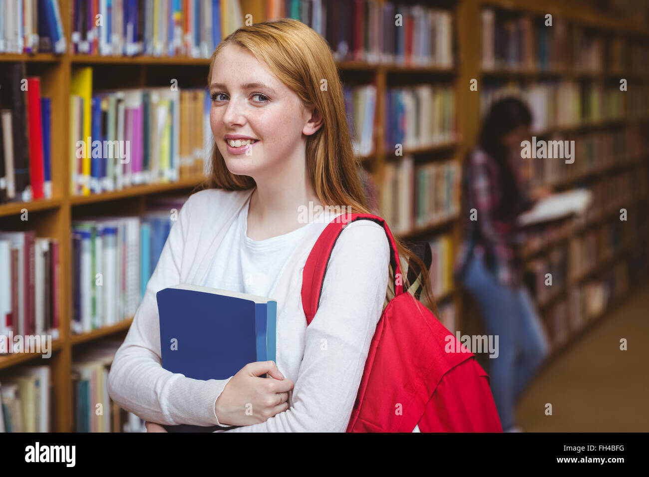 Smiling student with backpack holding a book in library Stock Photo - Alamy