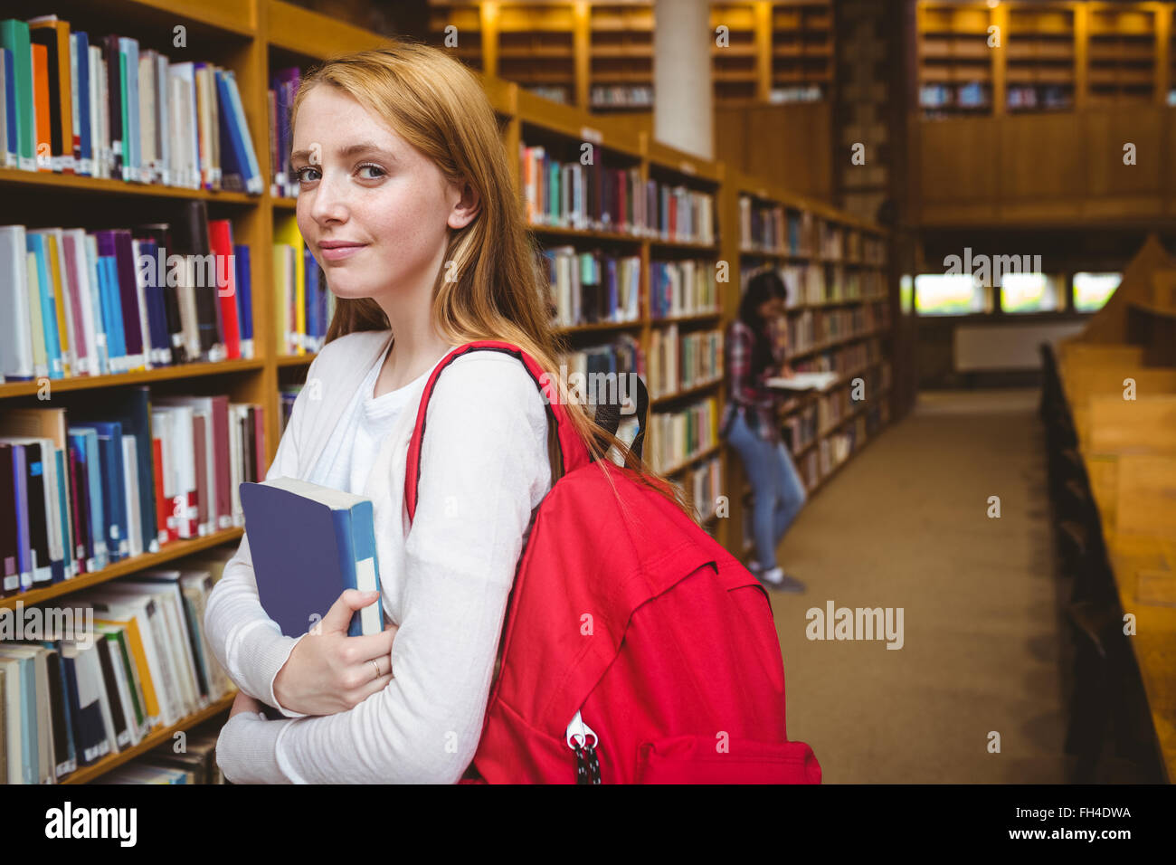 Smiling student with backpack holding a book in library Stock Photo - Alamy