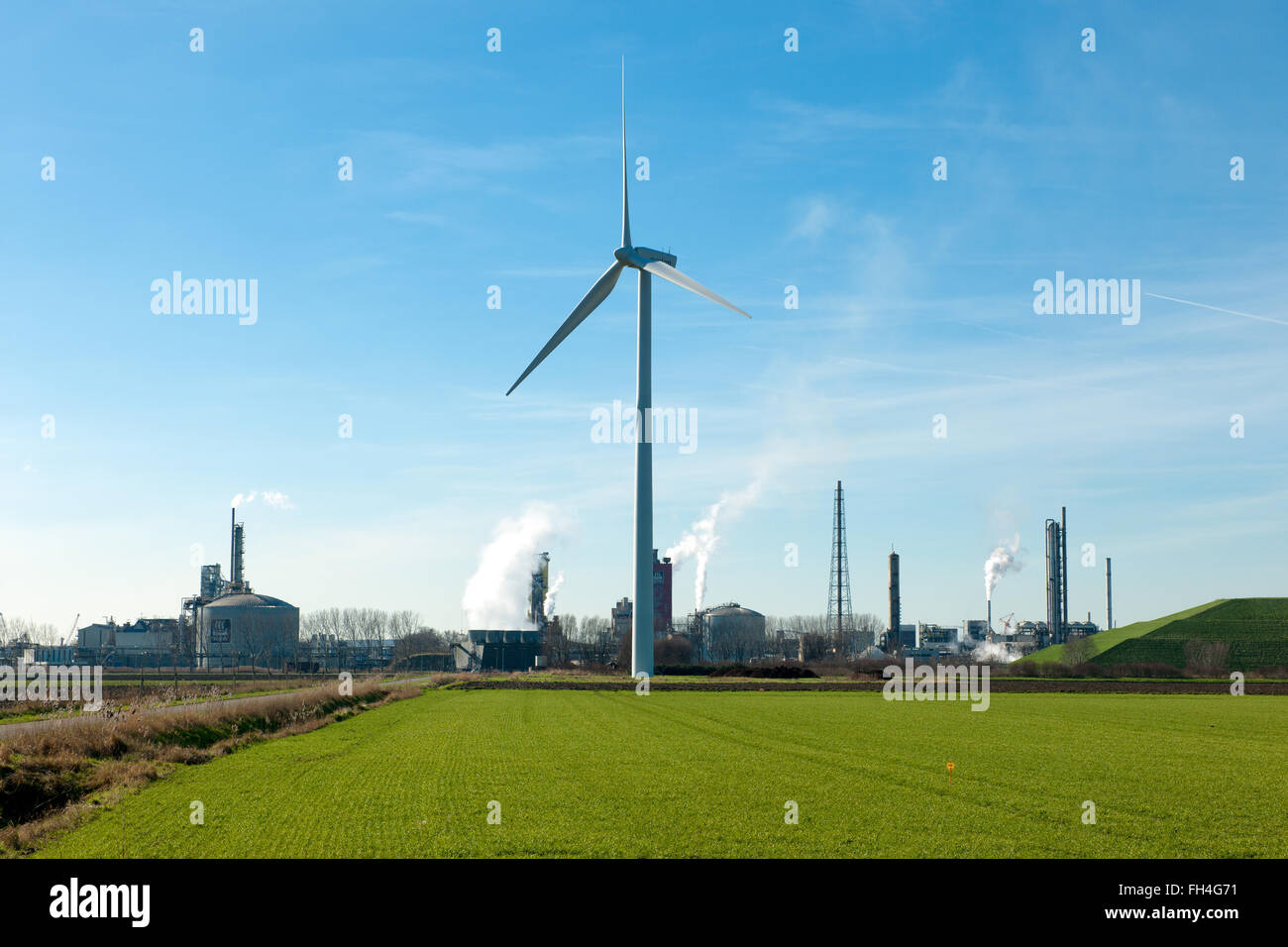Wind turbine on a green field with industrial Yara area in the background Stock Photo
