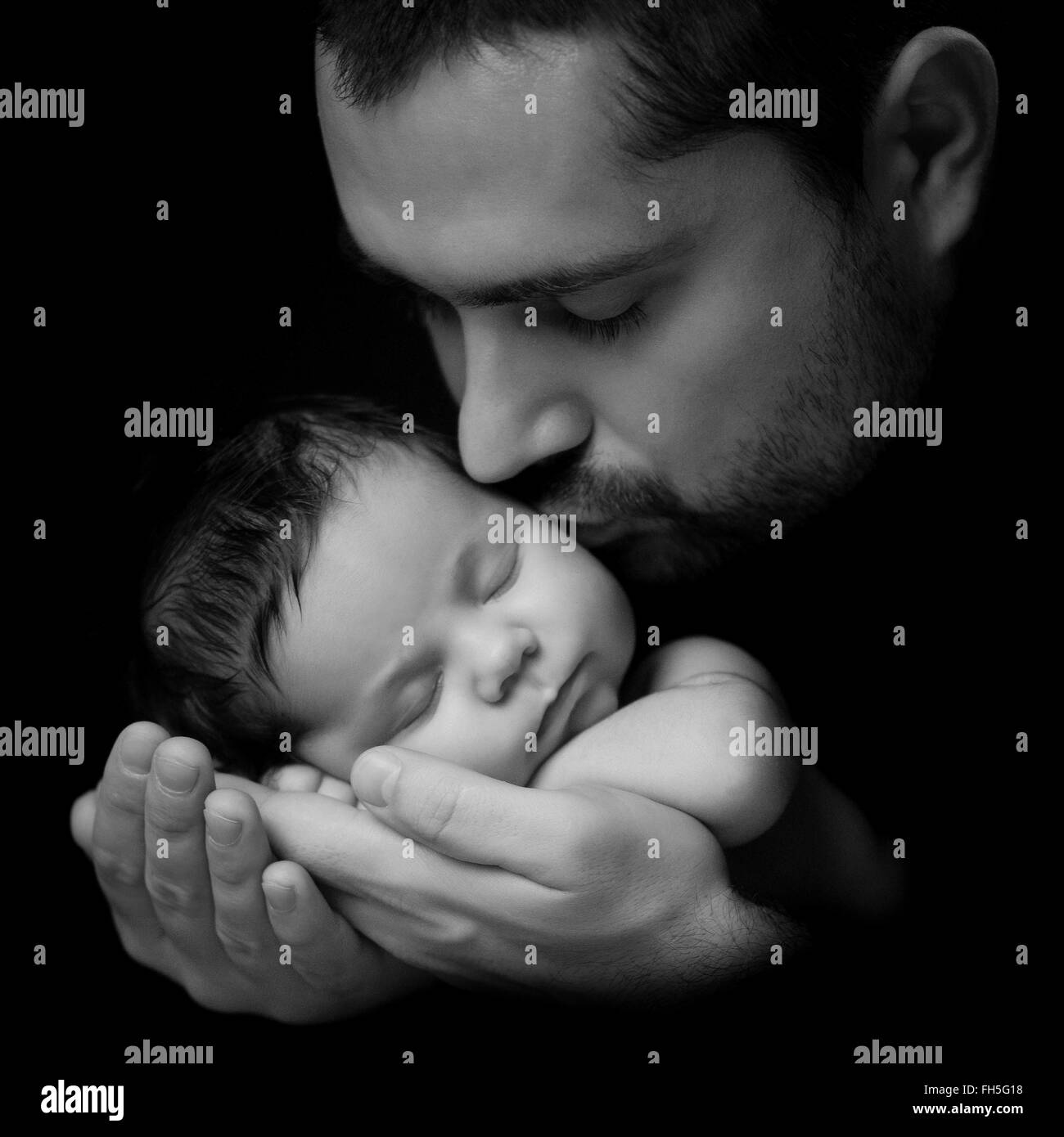 Father 's love.  Daddy kisses his newborn baby. Close-up portrait on a black background Stock Photo