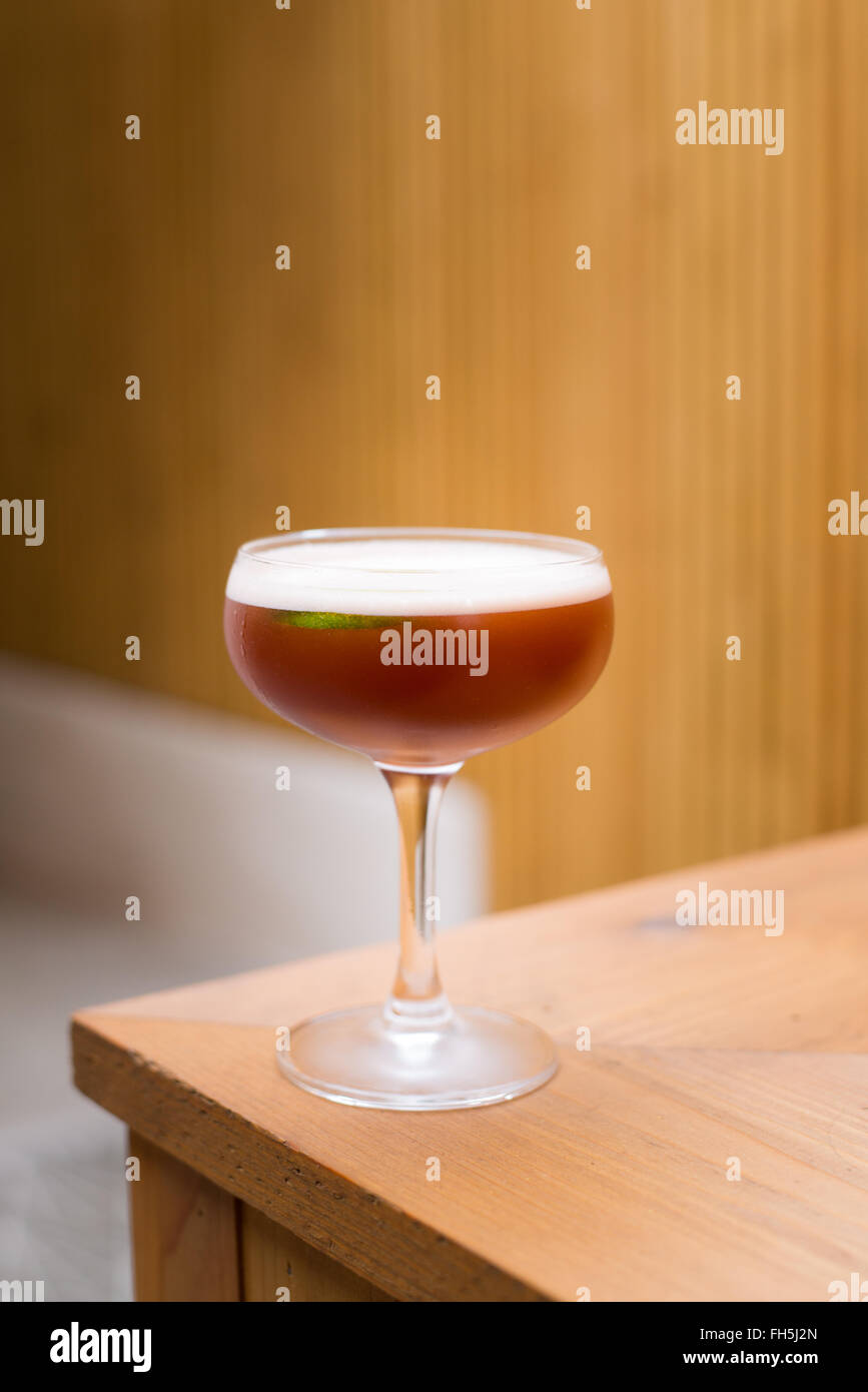 An eye-level view of a burgundy-colored cocktail in a stemmed glass, with a slight view of a life garnish. Stock Photo