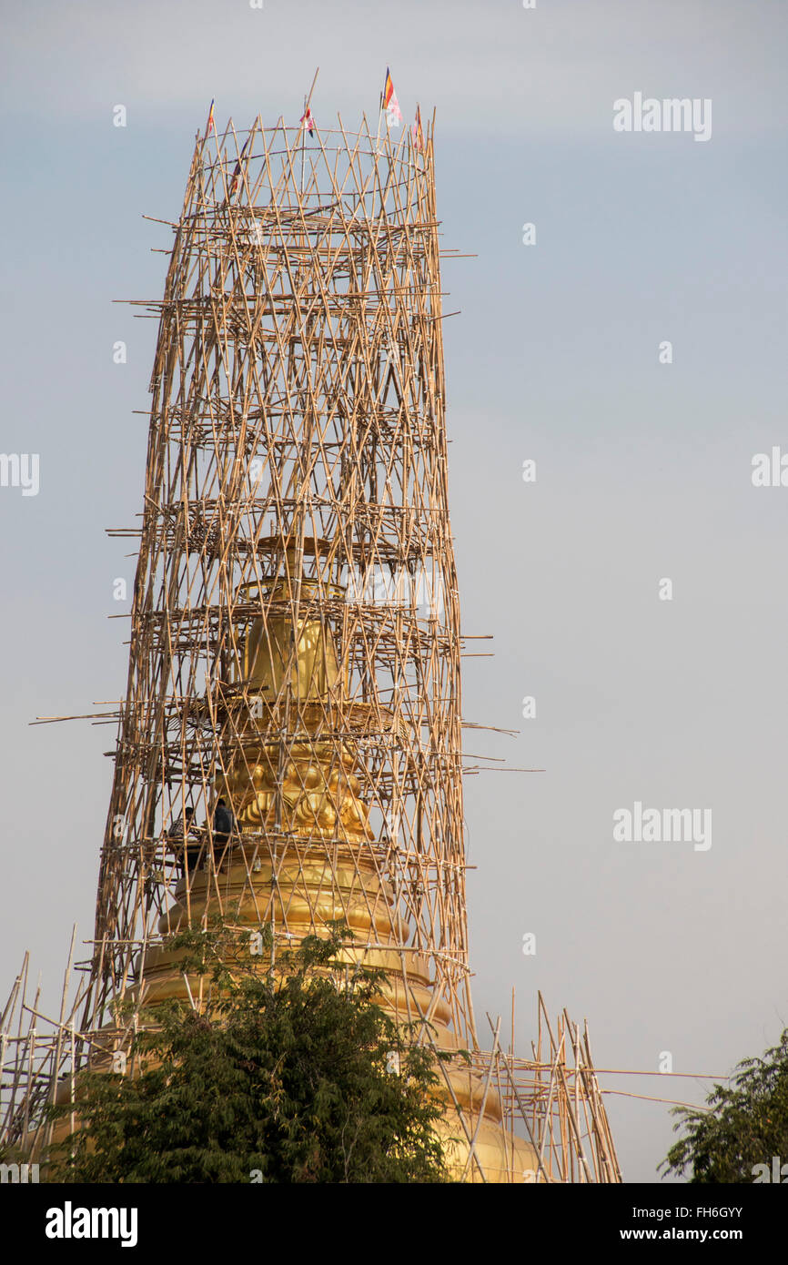 Workers apply gold leaf to regilt a chedi using bamboo scaffolding Mandalay,Myanmar Stock Photo