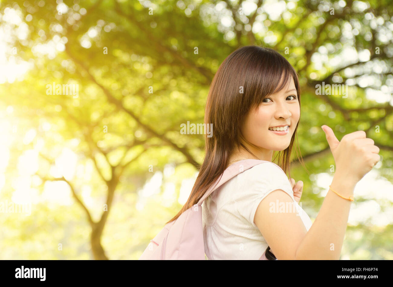 Young Asian university girl student standing on campus lawn, giving thumb up and smiling. Stock Photo