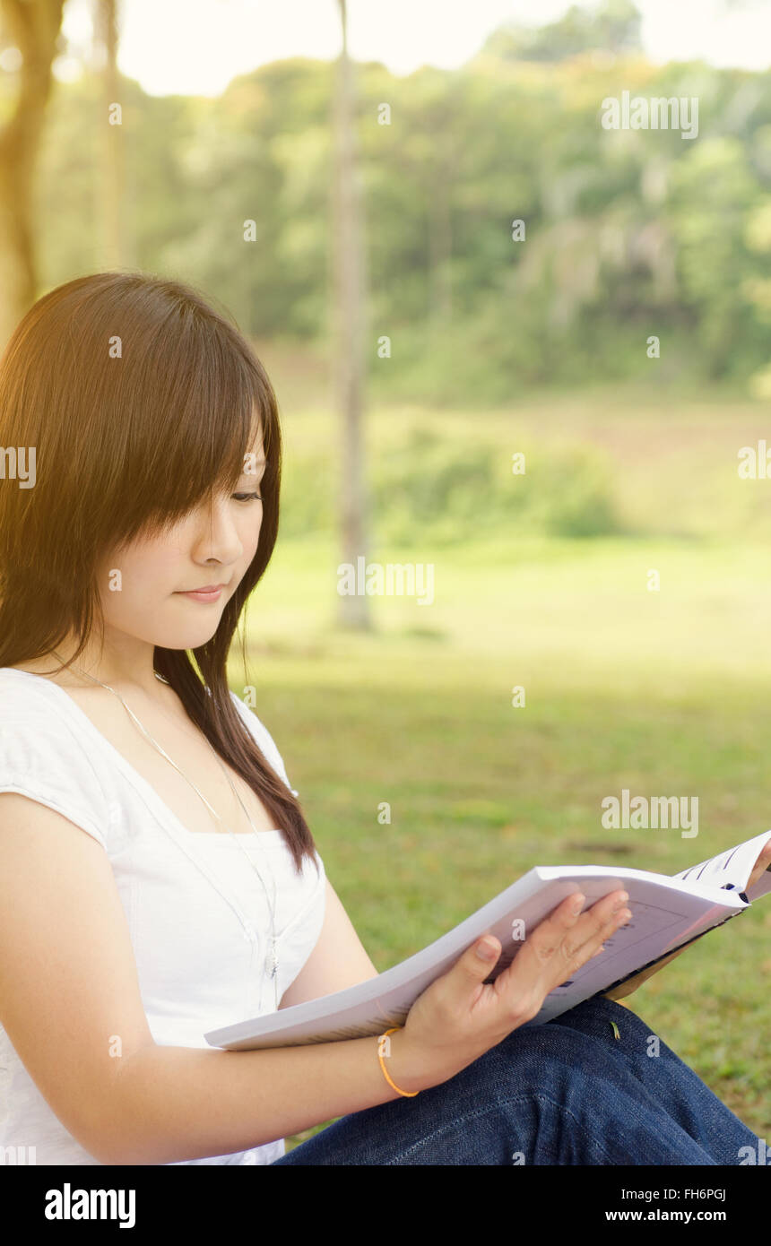 Young Asian college girl student sitting on campus lawn and reading ...