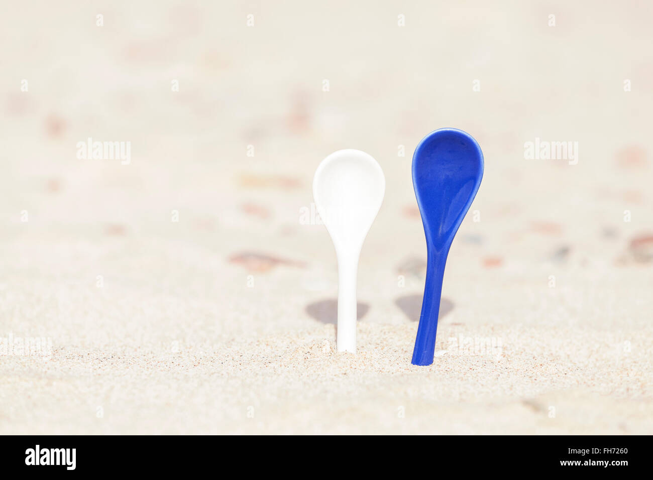 White and blue porcelain spoons stuck in sand. Stock Photo