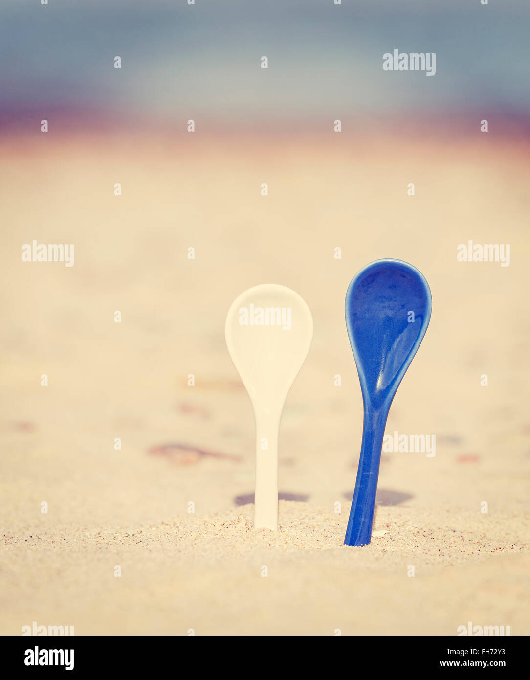 Vintage stylized two porcelain spoons stuck in sand. Stock Photo