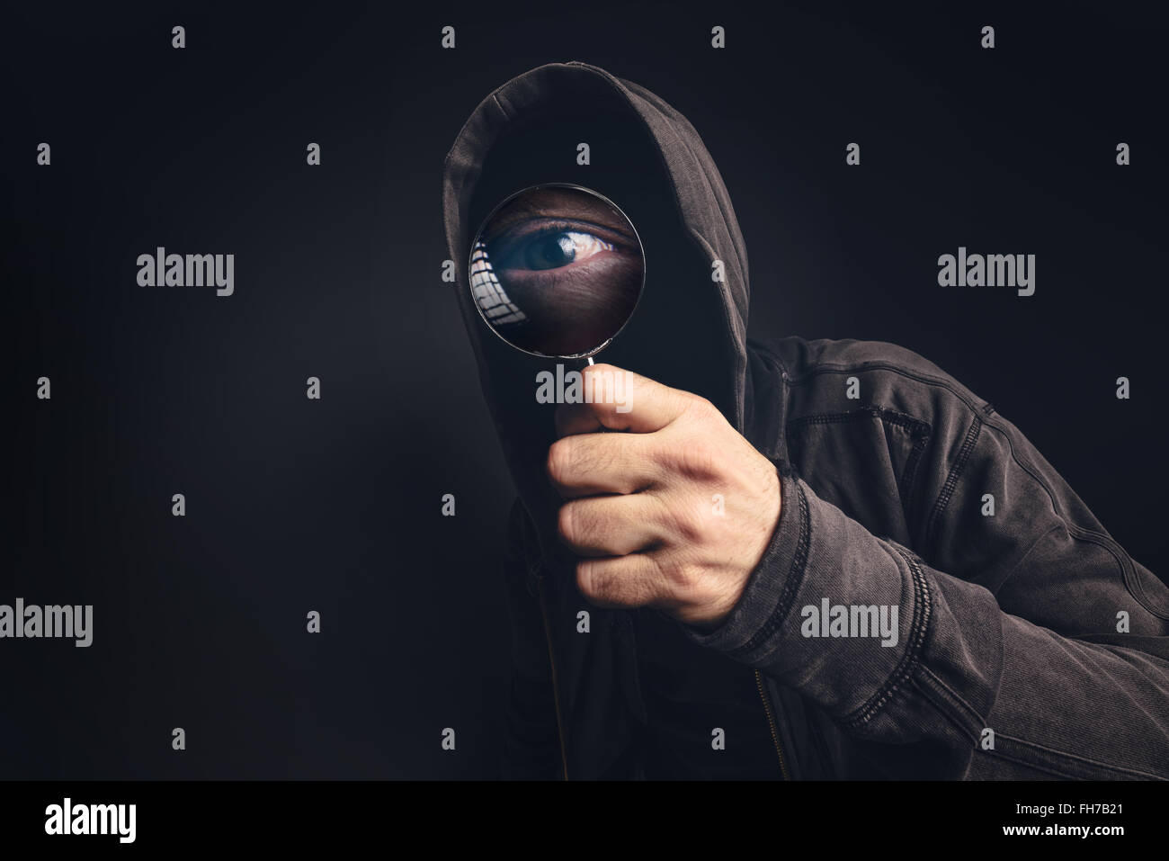 Bizarre hooded spooky person with magnifying glass, focus on enlarged eye peeking at you Stock Photo