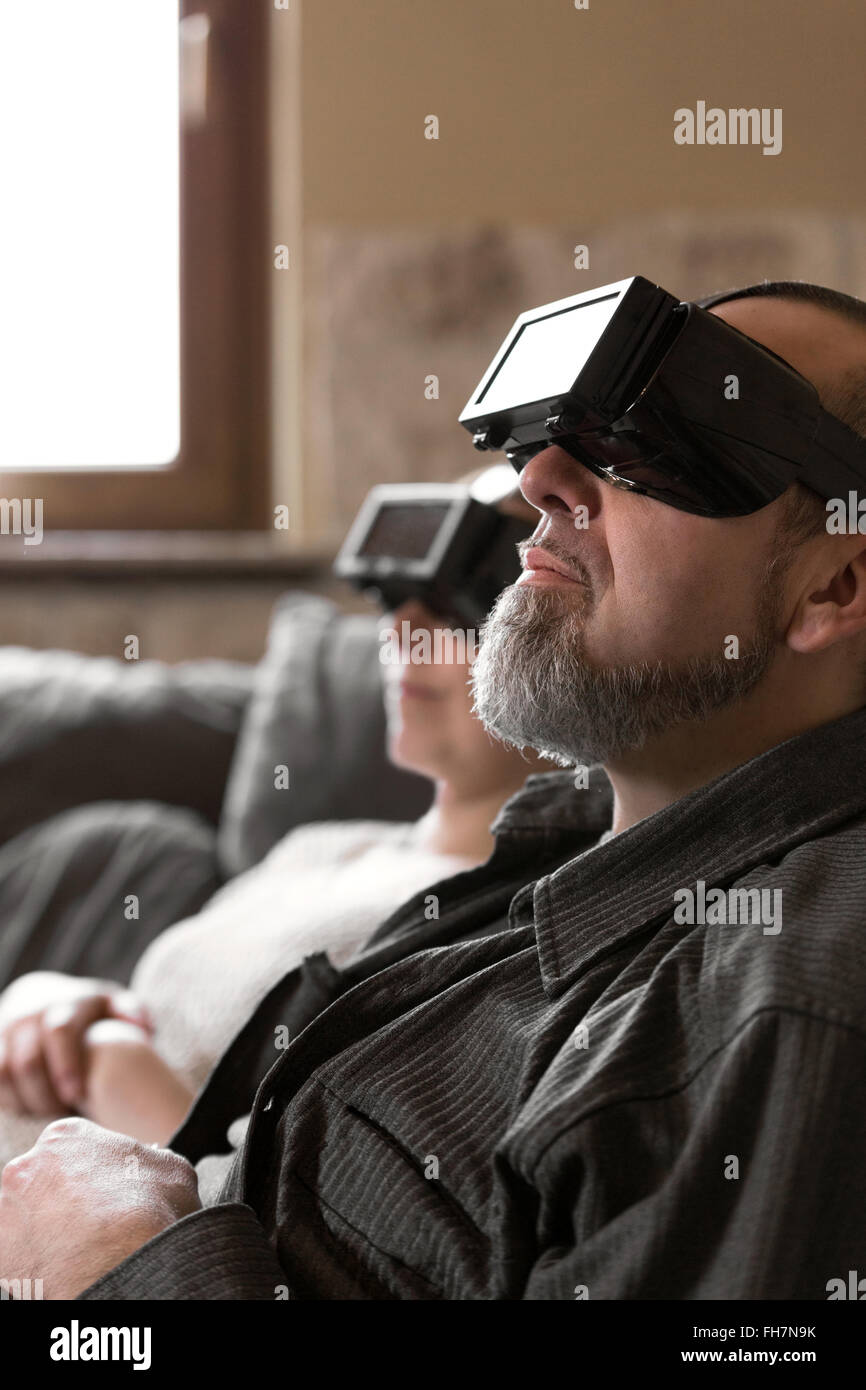 couple with virtual reality glasses is sitting on a couch Stock Photo