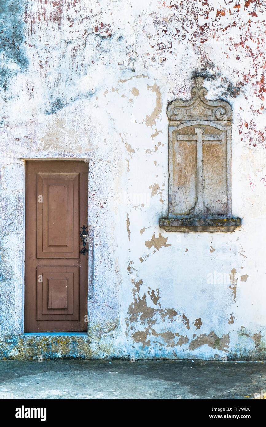 wall with door and stone relief in the form of a window bearing a cross Stock Photo