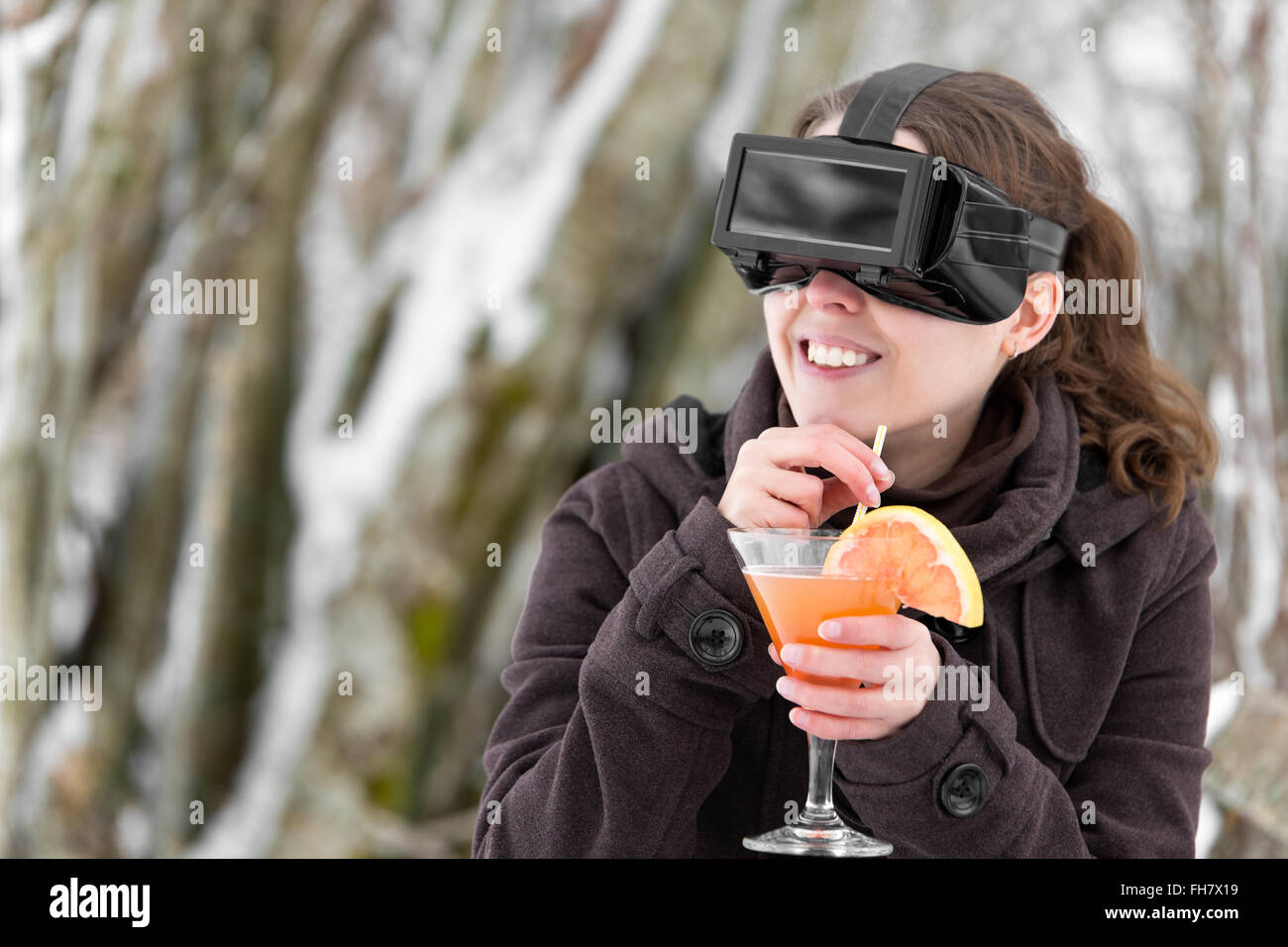 woman in snow is wearing virtual reality glasses and dreaming of summer with a cocktail in her hand Stock Photo