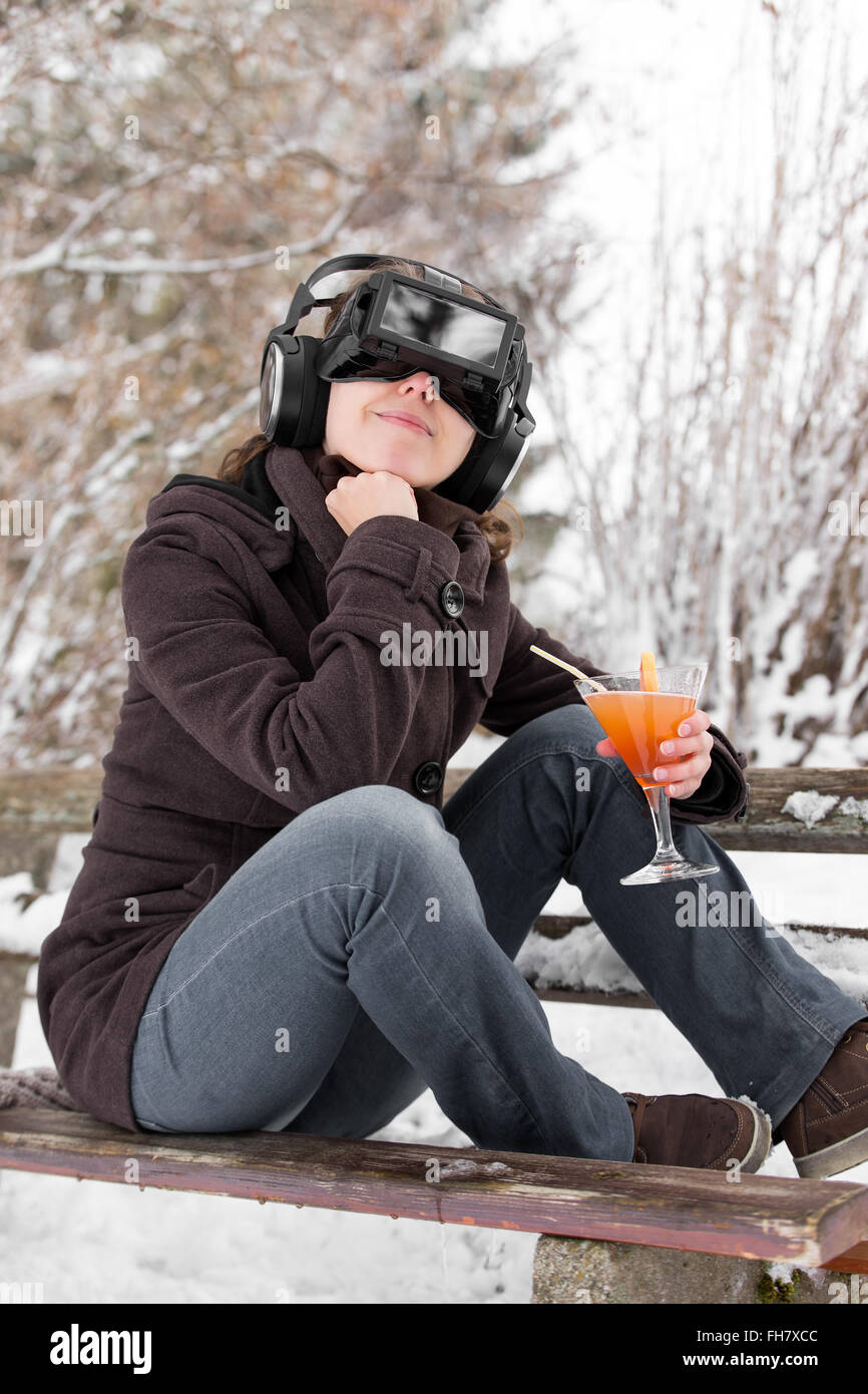 woman in snow is wearing virtual reality glasses and dreaming of summer holiday with a cocktail in her hand Stock Photo