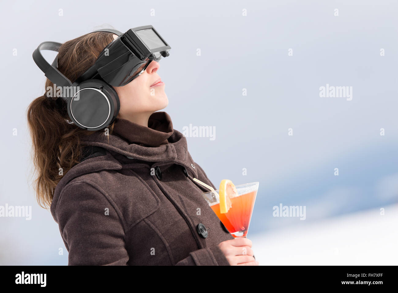woman in snow is wearing virtual reality glasses and dreams of summer holiday with a cocktail in her hand Stock Photo