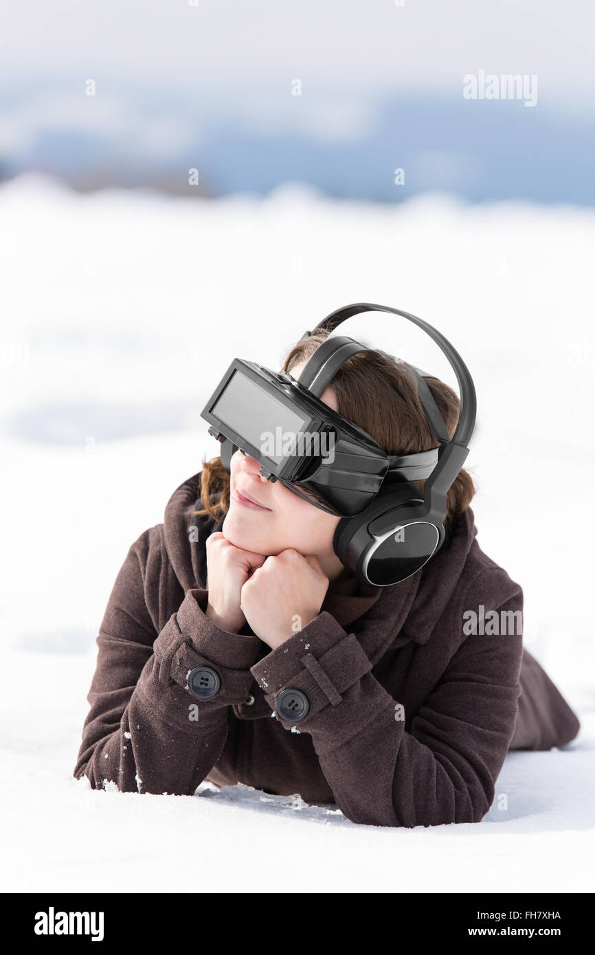 young pretty woman is laying in the snow, wearing virtual reality glasses Stock Photo