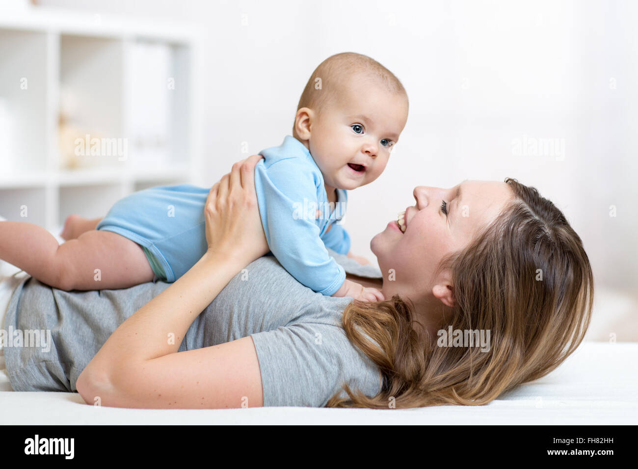 Happy mother and baby hug and play lying indoors Stock Photo