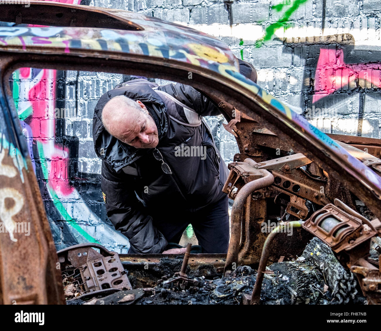 Güterbahnhof train station, Pankow, Berlin. Old man looks at burnt out car in fire damaged garage at disused freight rail yard Stock Photo