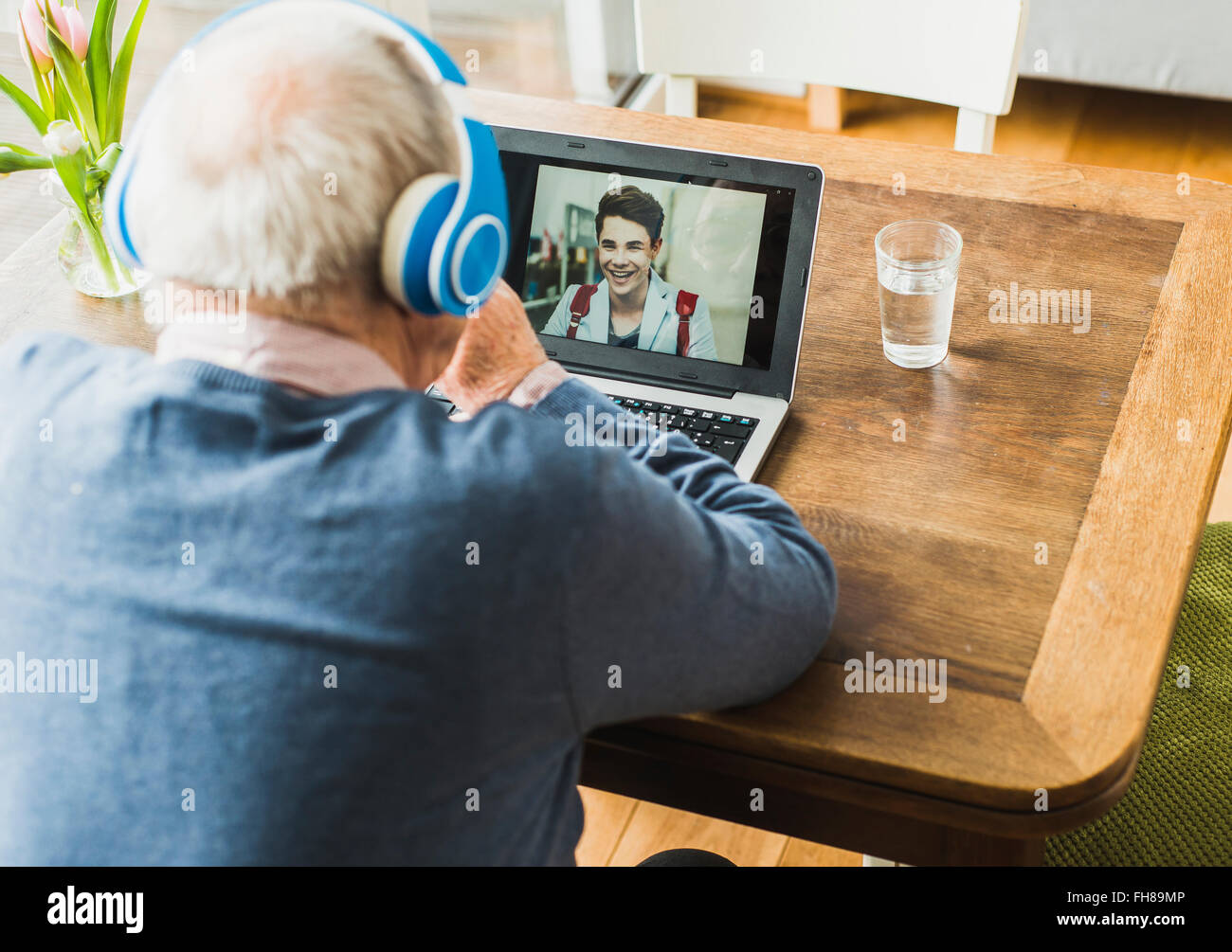 Senior man using laptop and headphones for skyping with his grandson Stock Photo