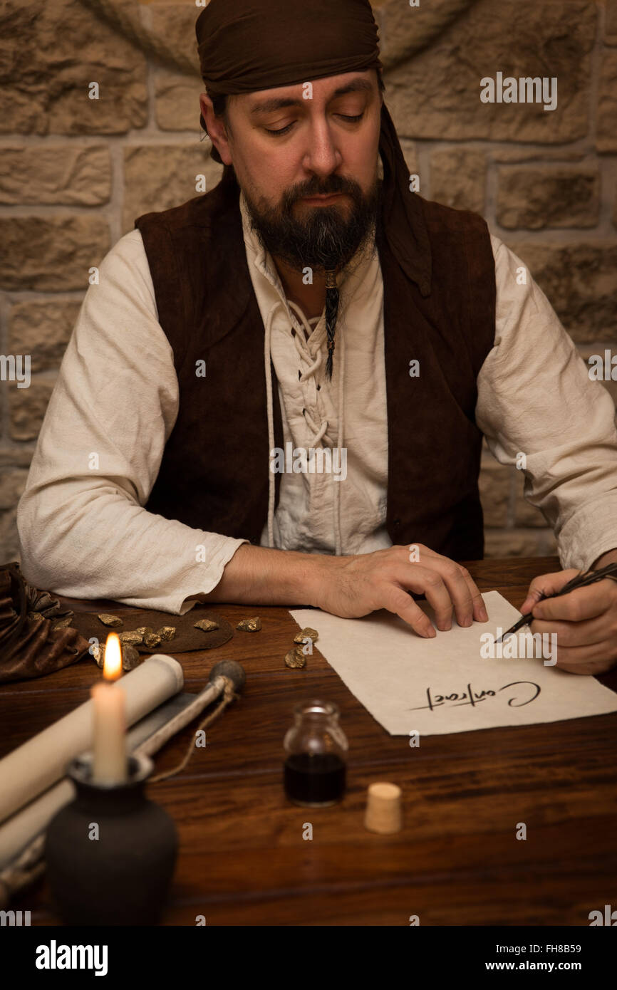 Medieval man sitting on a old table and sign a contract Stock Photo