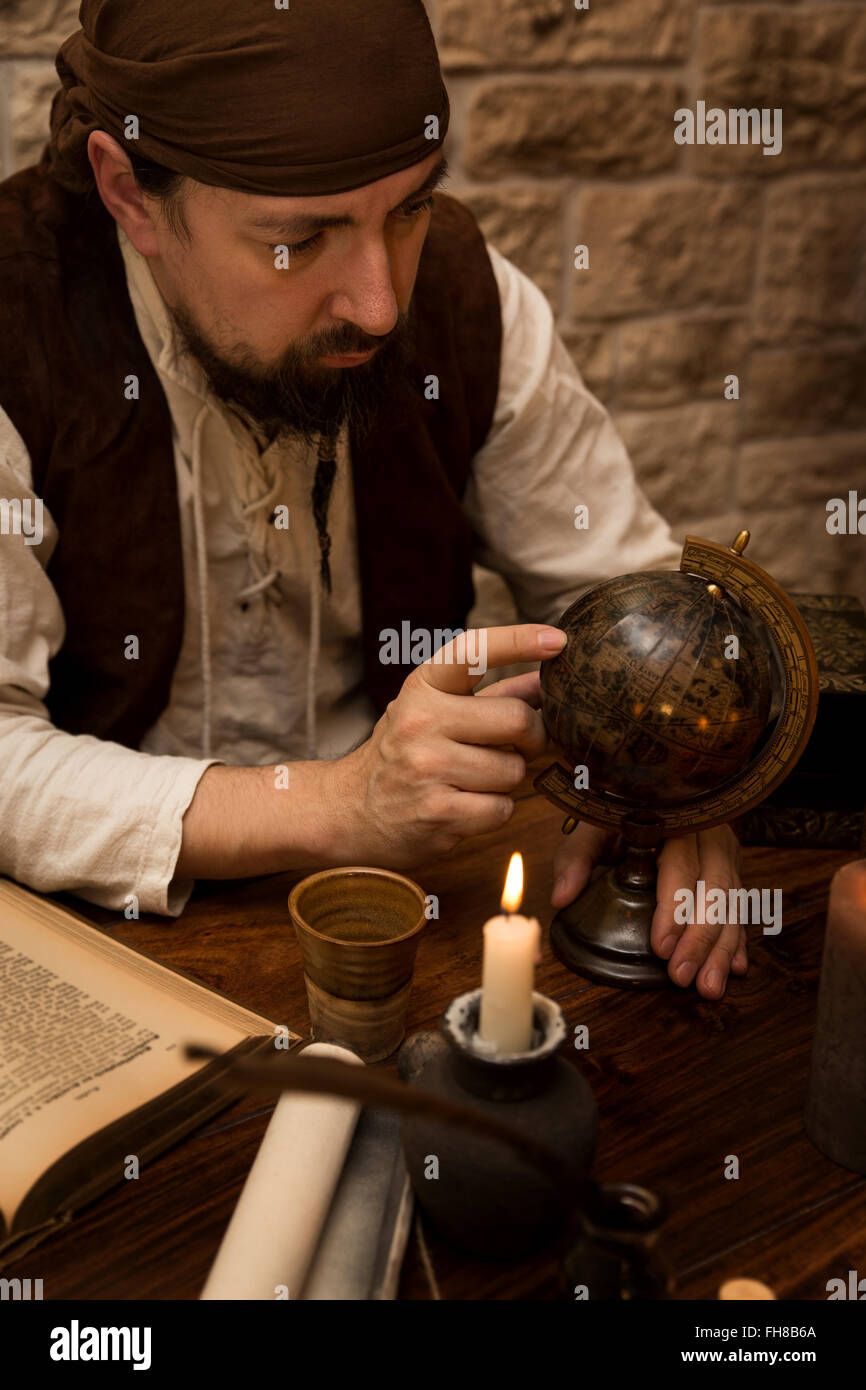 a medieval man pointing at a old globe, concept traveling and tourism Stock Photo
