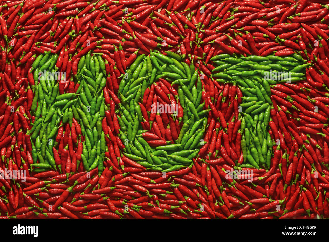 Word HOT written with green peppers, amid red peppers. Stock Photo