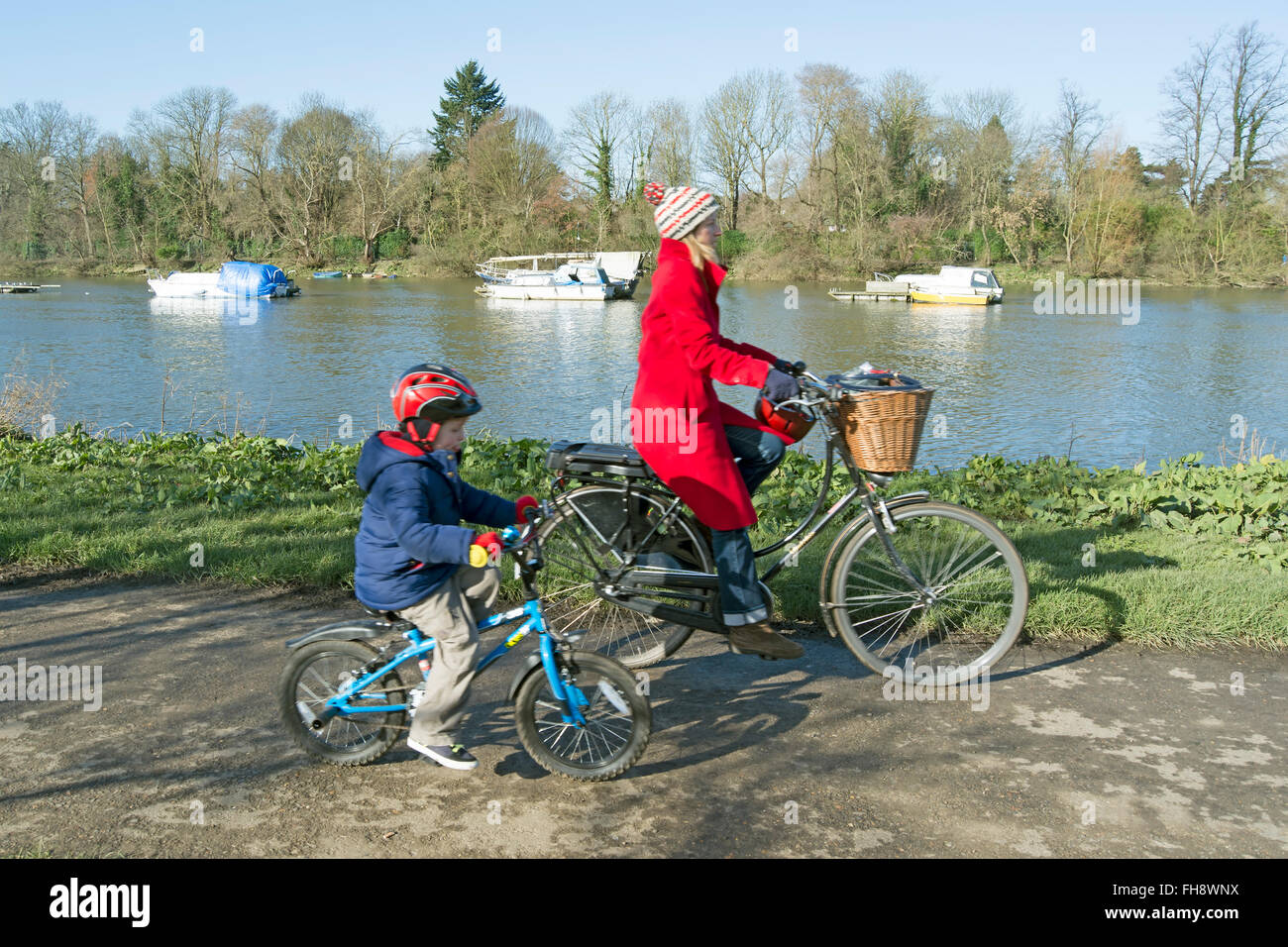 woman and young boy ride bicycles alongside the river thames in ham, surrey, england Stock Photo