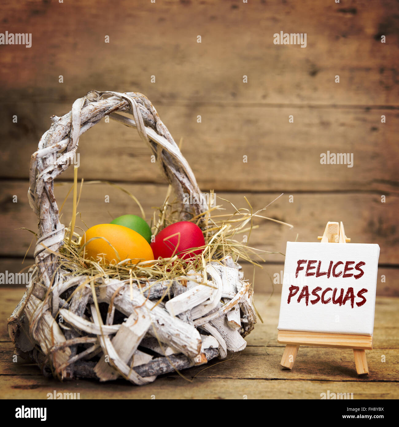 white basket with easter eggs, canvas with spanish text felices pascuas, which means happy easter, wooden background Stock Photo