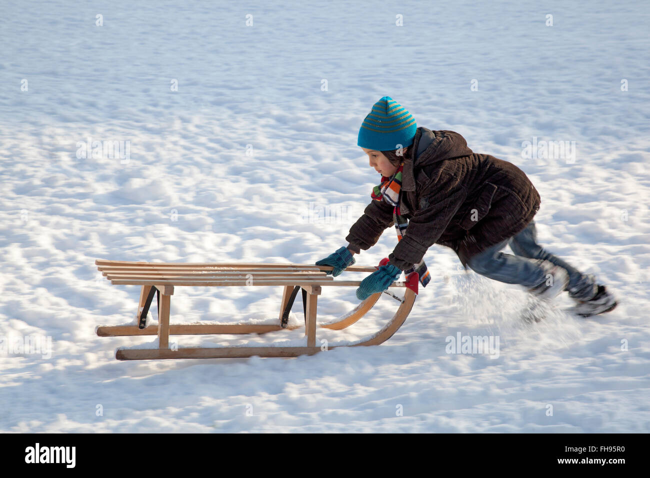 Little boy pushing sled uphills in the snow Stock Photo