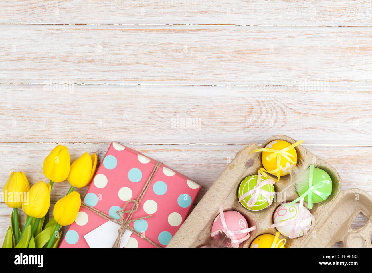 Easter background with colorful eggs and yellow tulips over white wood ...