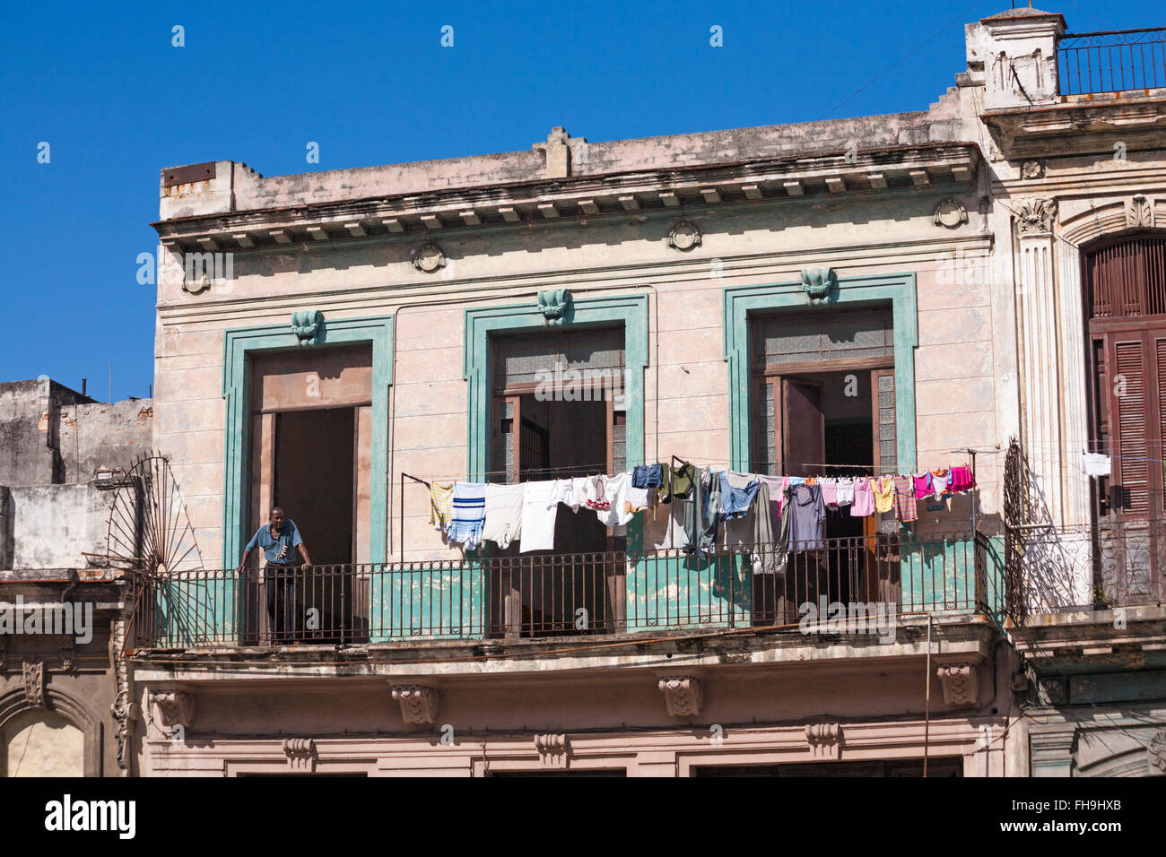 Daily life in Cuba - Cuban man with clothes pegs on t-shirt leaning on balcony railings with washing on line drying at Havana, Cuba, West Indies Stock Photo