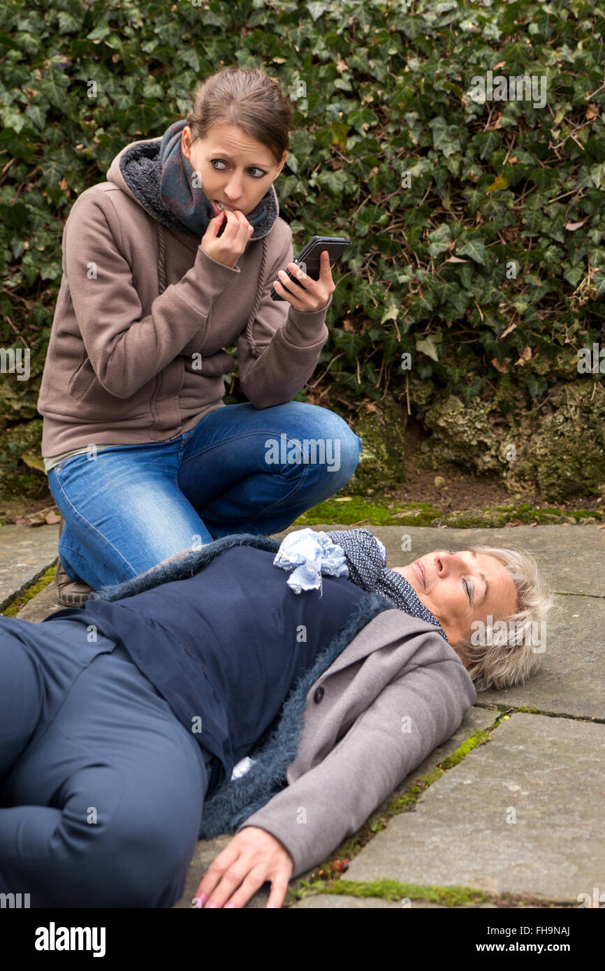 young woman do an emergency call, cause a senior adult is lying on the ground Stock Photo