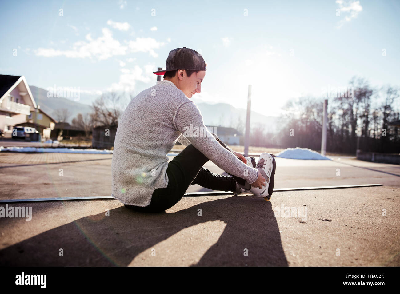 Young man sitting on ramp putting on inline skates Stock Photo