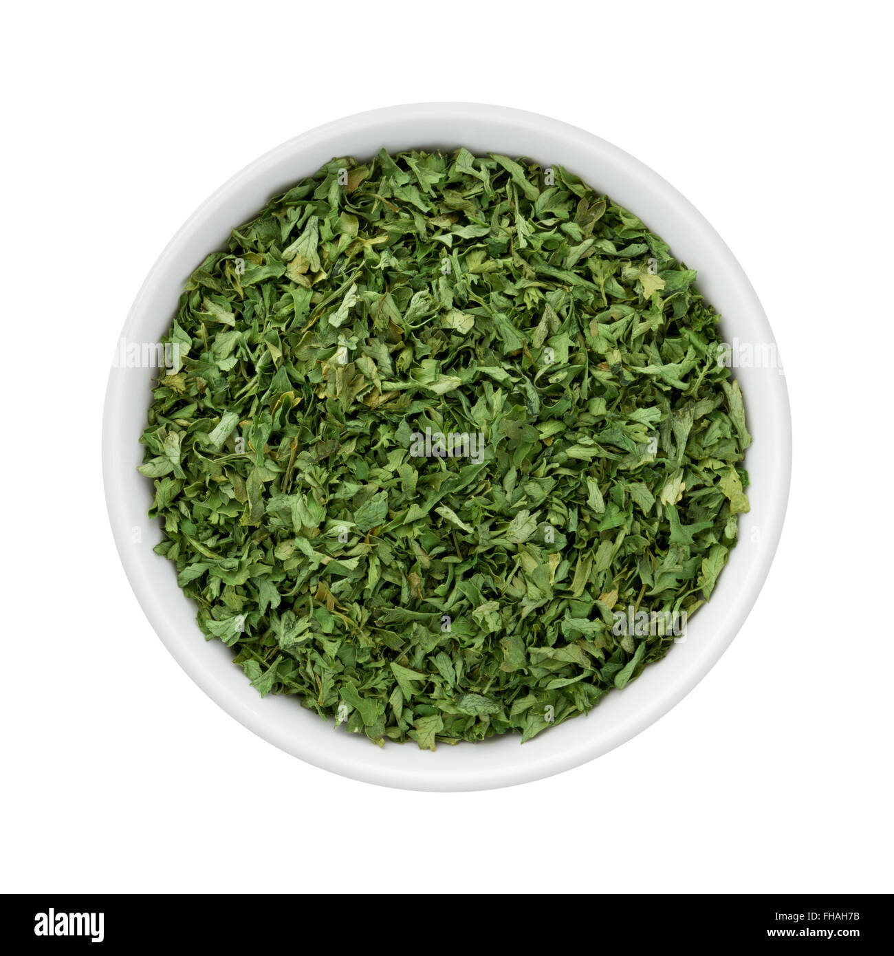 Dried Parsley Flakes in a Ceramic Bowl. The image is a cut out, isolated on a white background. Stock Photo