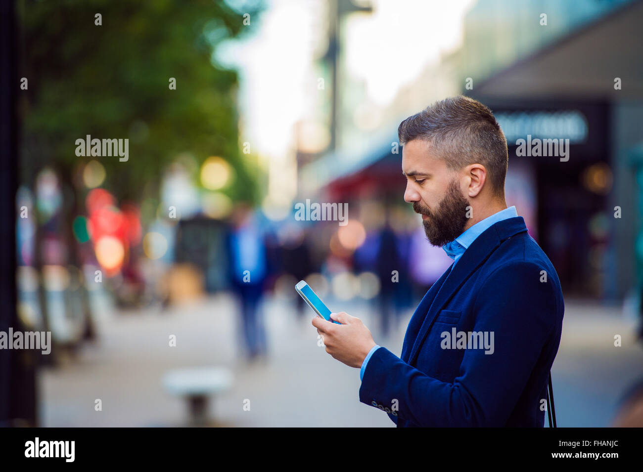 Hipster manager holding smartphone, texting outside in the stree Stock Photo