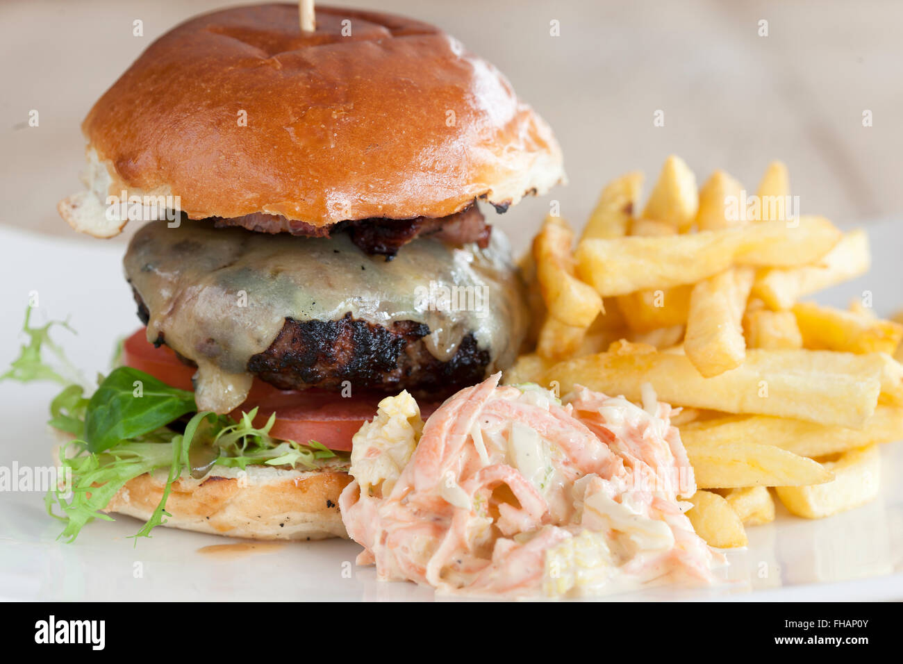 A beef burger with cheese, tomato and lettuce served with fries and coleslaw Stock Photo