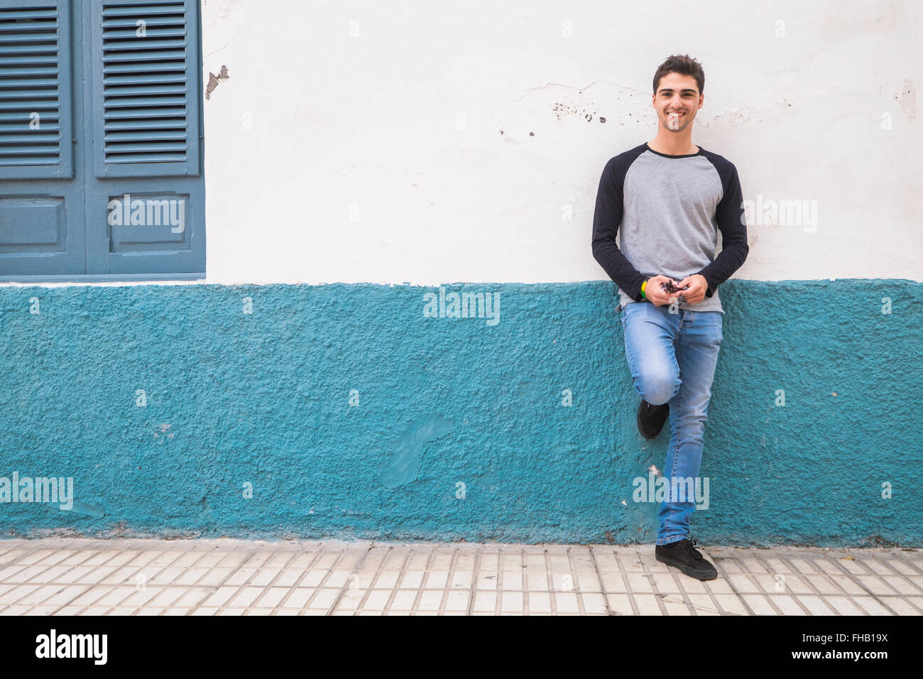 Smiling young man leaning against a wall Stock Photo - Alamy