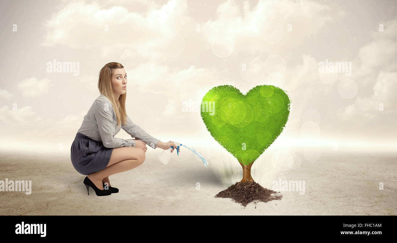 Business woman watering heart shaped green tree Stock Photo