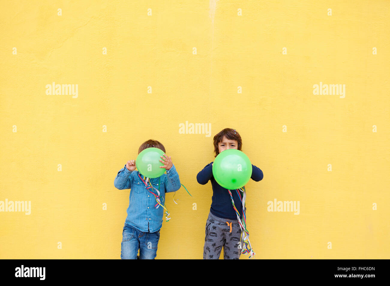 Two little boys with green balloons and streamers standing in front of ...