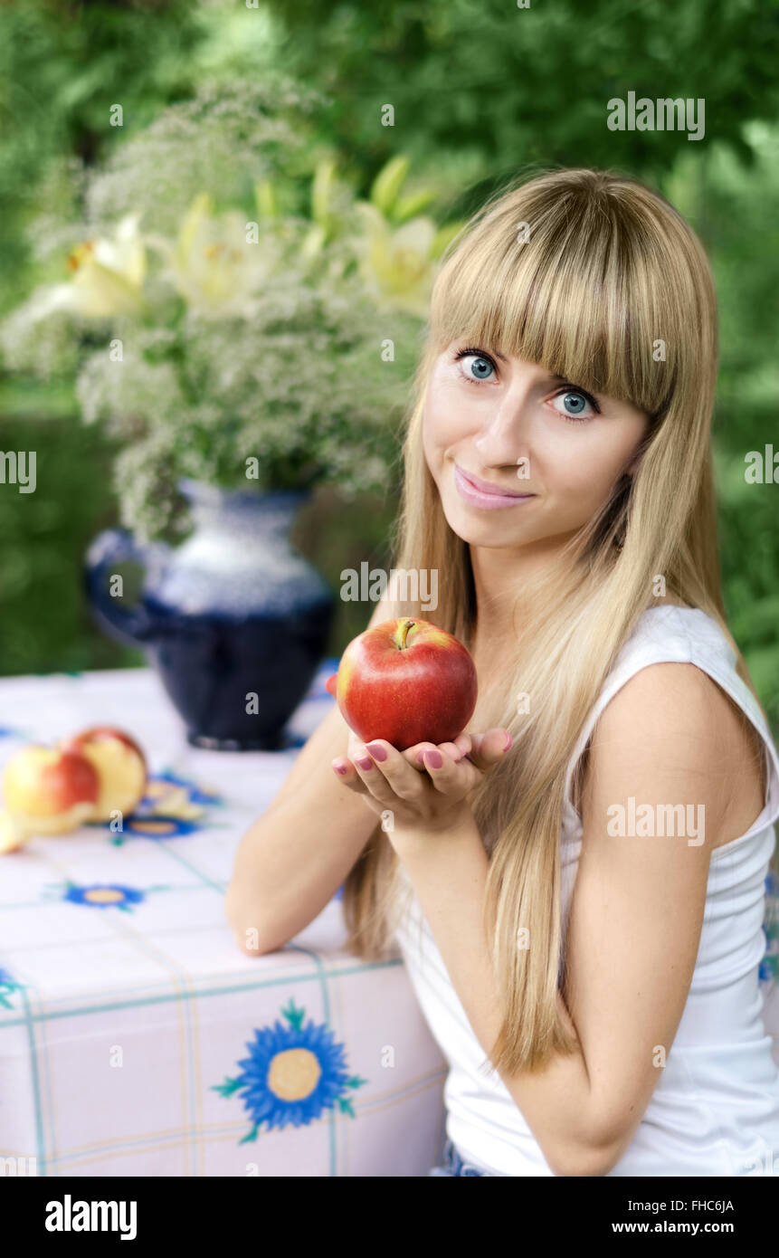 Girl holding Apple, sitting at a table in the garden Stock Photo