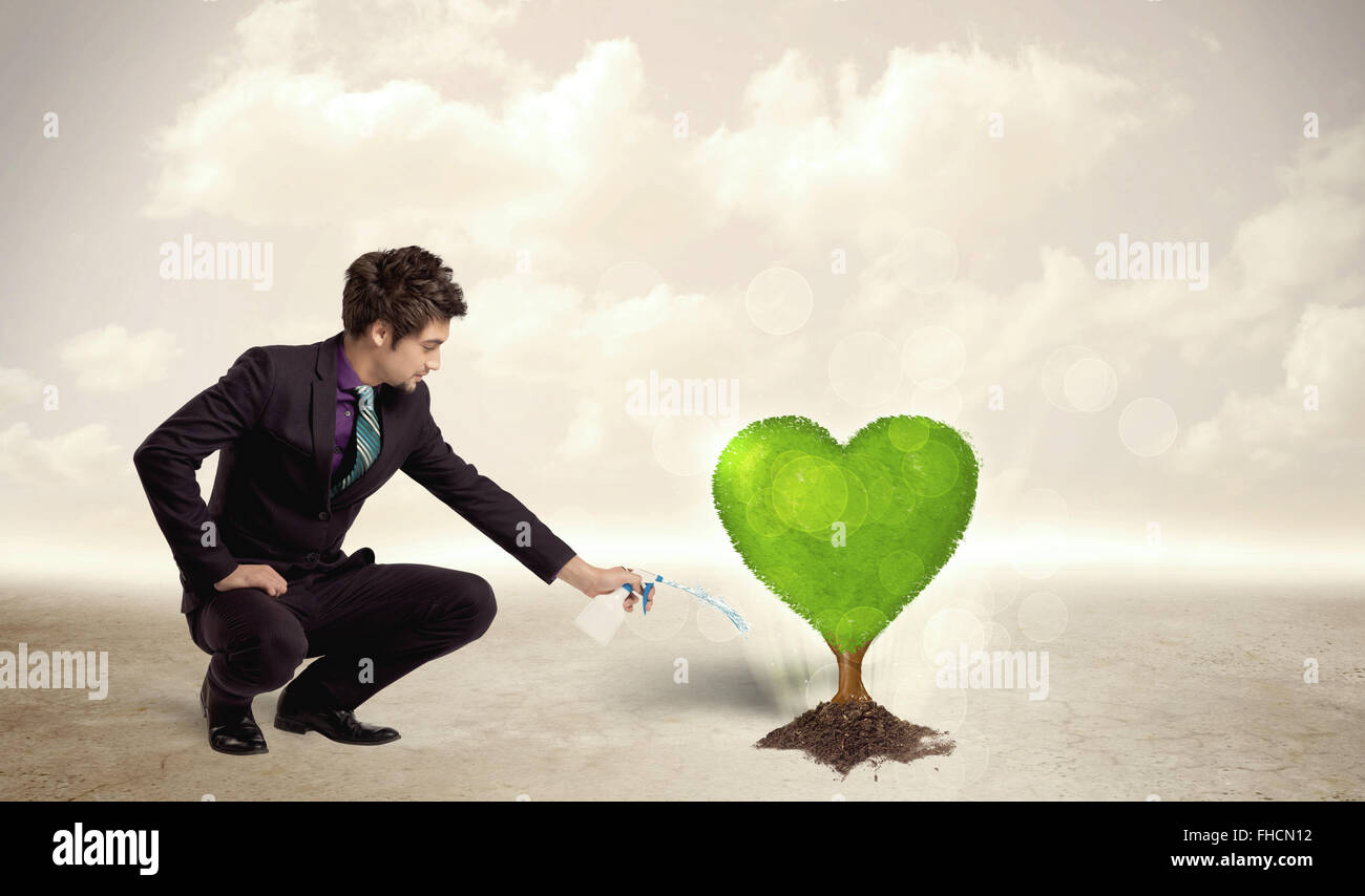 Business man watering heart shaped green tree Stock Photo