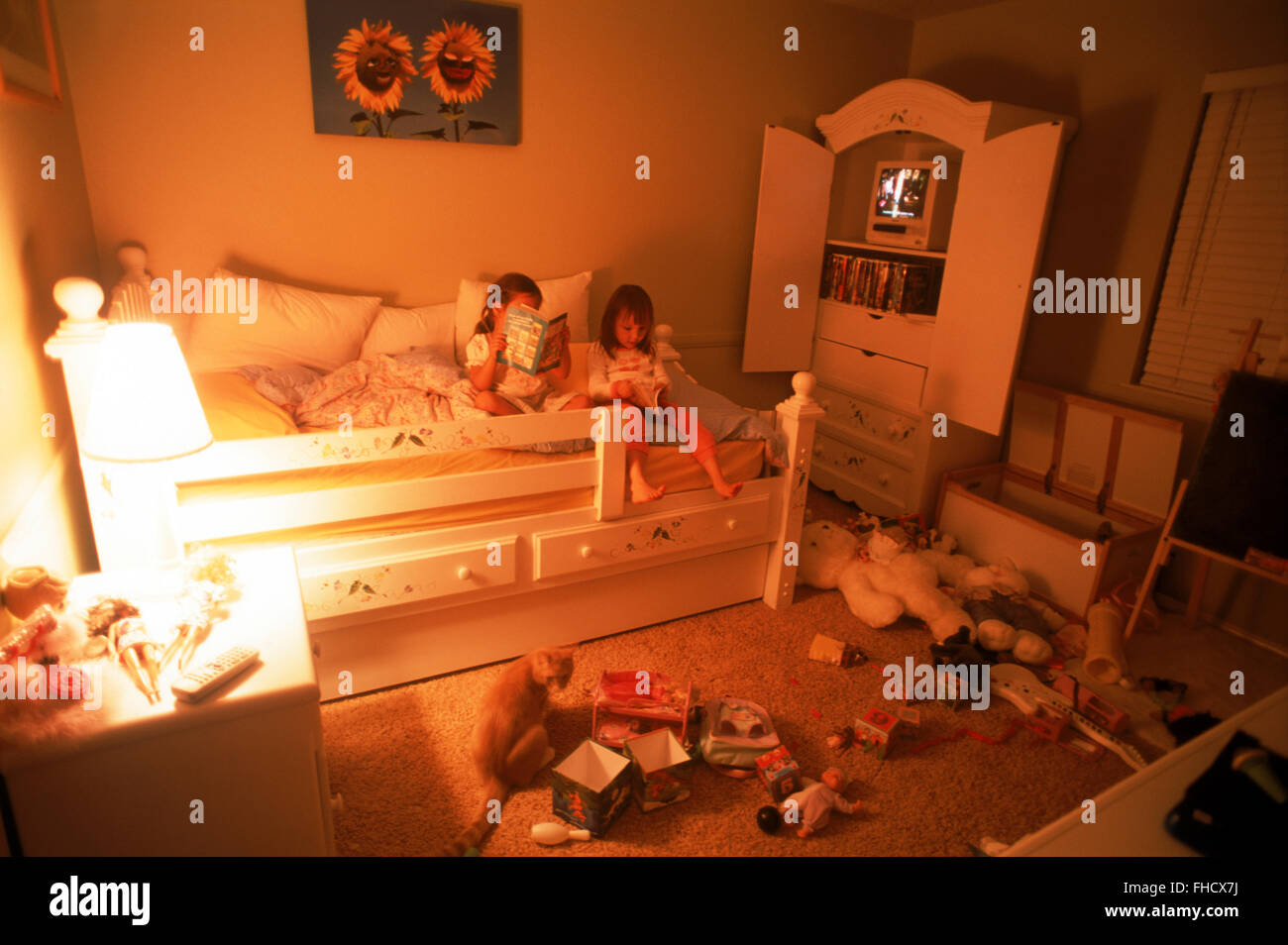 Two young girls in bedroom amid messy sea of toys Stock Photo