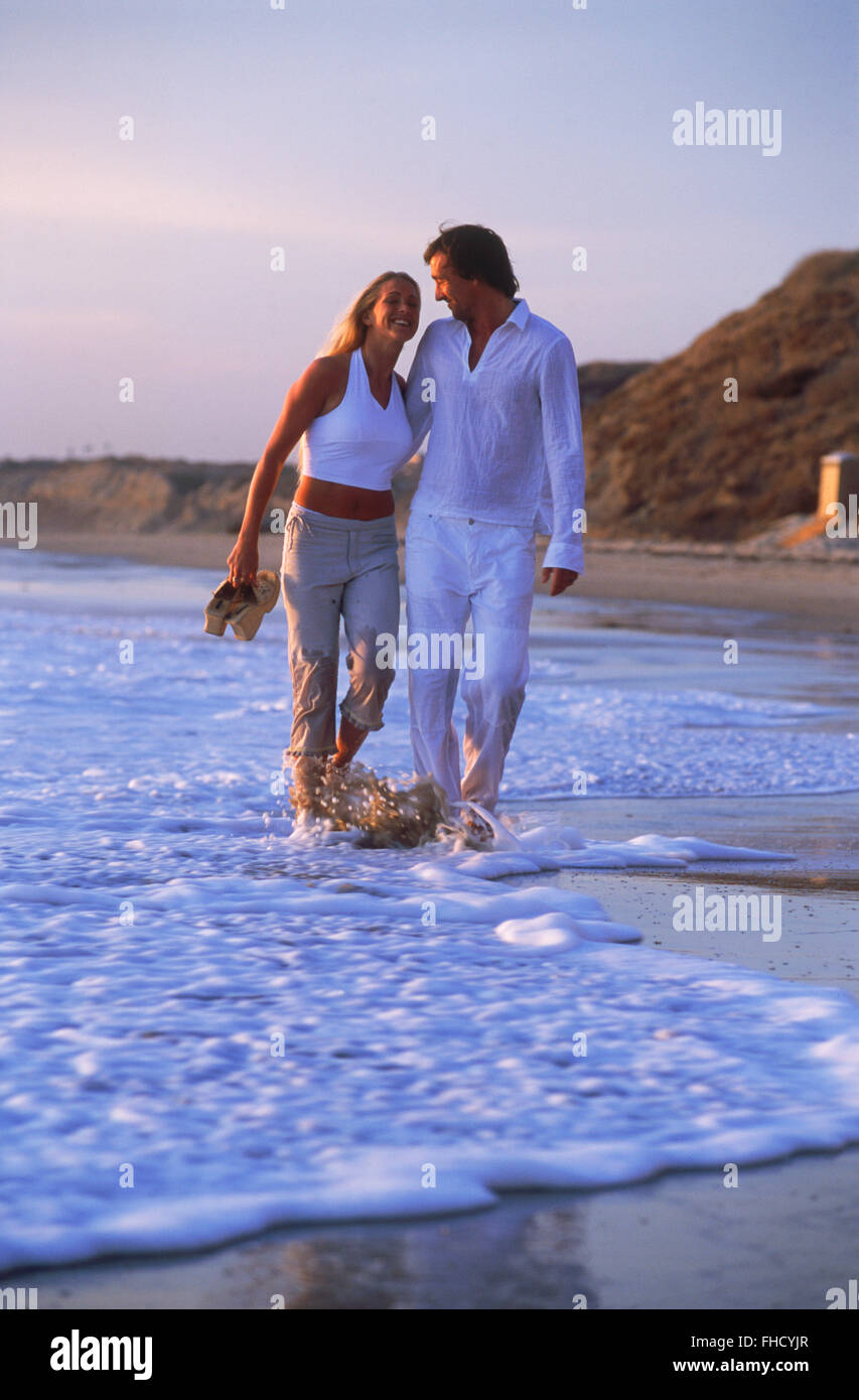 Couple in love enjoying romantic walk through beach waves along California shore at sunset Stock Photo