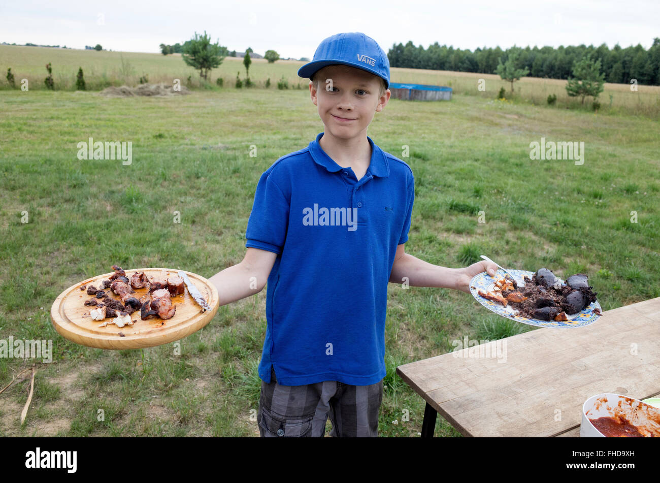 Polish boy age 12 holds up platters of freshly cooked kielbasa & blood sausage he cooked at outside grill Zawady Central Poland Stock Photo