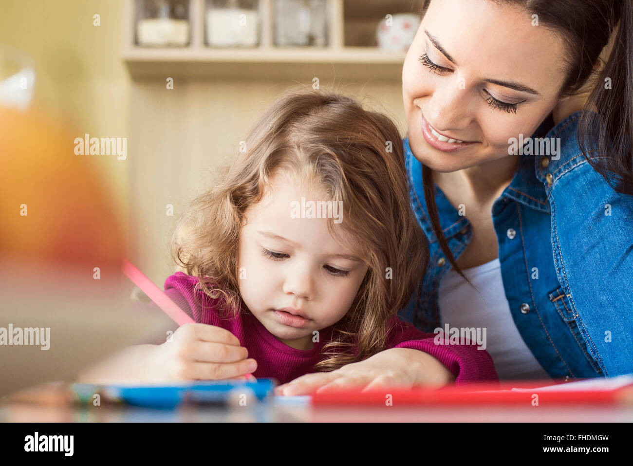 Portrait of little girl painting with coloured pencils while mother is ...